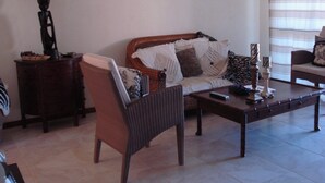 A living room with a sofa, armchair, coffee table, and a lamp. There are two wall-mounted pictures and a window with blinds.
