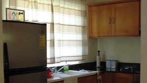 A kitchen with wooden cabinets, a stainless steel refrigerator, a window with a striped curtain, and a sink.