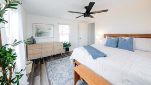 A bedroom with a bed, bedside table, nightstand, dresser, and a ceiling fan.
