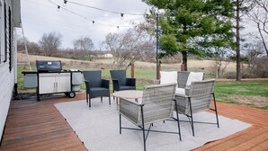 An outdoor deck with wicker furniture, a grill, and string lights.