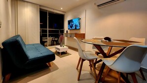 A modern living room with a sofa, a glass dining table with chairs, a TV mounted on the wall, and an air conditioning unit. - New and with ocean view (Cartagena)