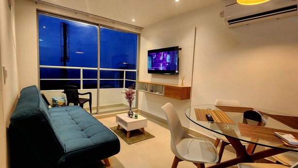 A modern living room with a sofa, a glass dining table, chairs, a TV, and a balcony with a view. - New and with ocean view (Cartagena)