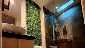 A modern bathroom with a white toilet, a wooden vanity, a green vertical garden, and a glass shower enclosure. - New and with ocean view (Cartagena)