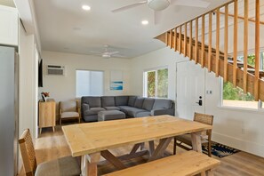 Una sala de estar moderna con una mesa de comedor de madera, un sofá seccional gris y una escalera con barandilla de madera.