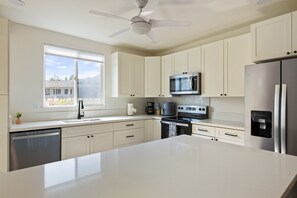 Una cocina moderna con gabinetes blancos, electrodomésticos de acero inoxidable, una isla grande y un ventilador de techo.