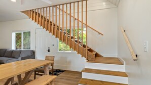 A modern interior with a wooden staircase, a dining area with a wooden table and benches, and a gray sofa. - Hale Kai Bungalow - New Build on the beach! (Laie)