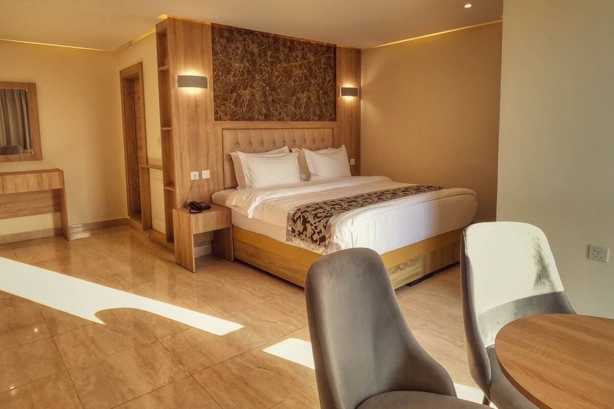 Una habitación de hotel moderna con una cama grande, cabecera de madera, un escritorio y dos sillas.