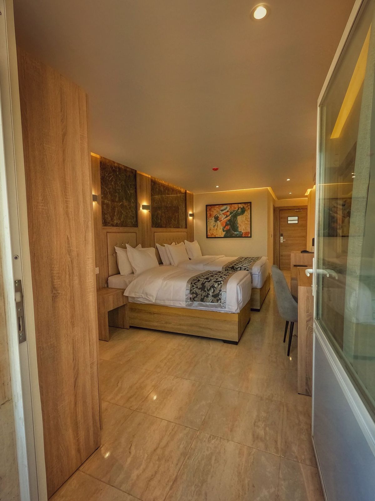 A modern bedroom with a wooden bed frame, two beds, a desk, and a glass partition.