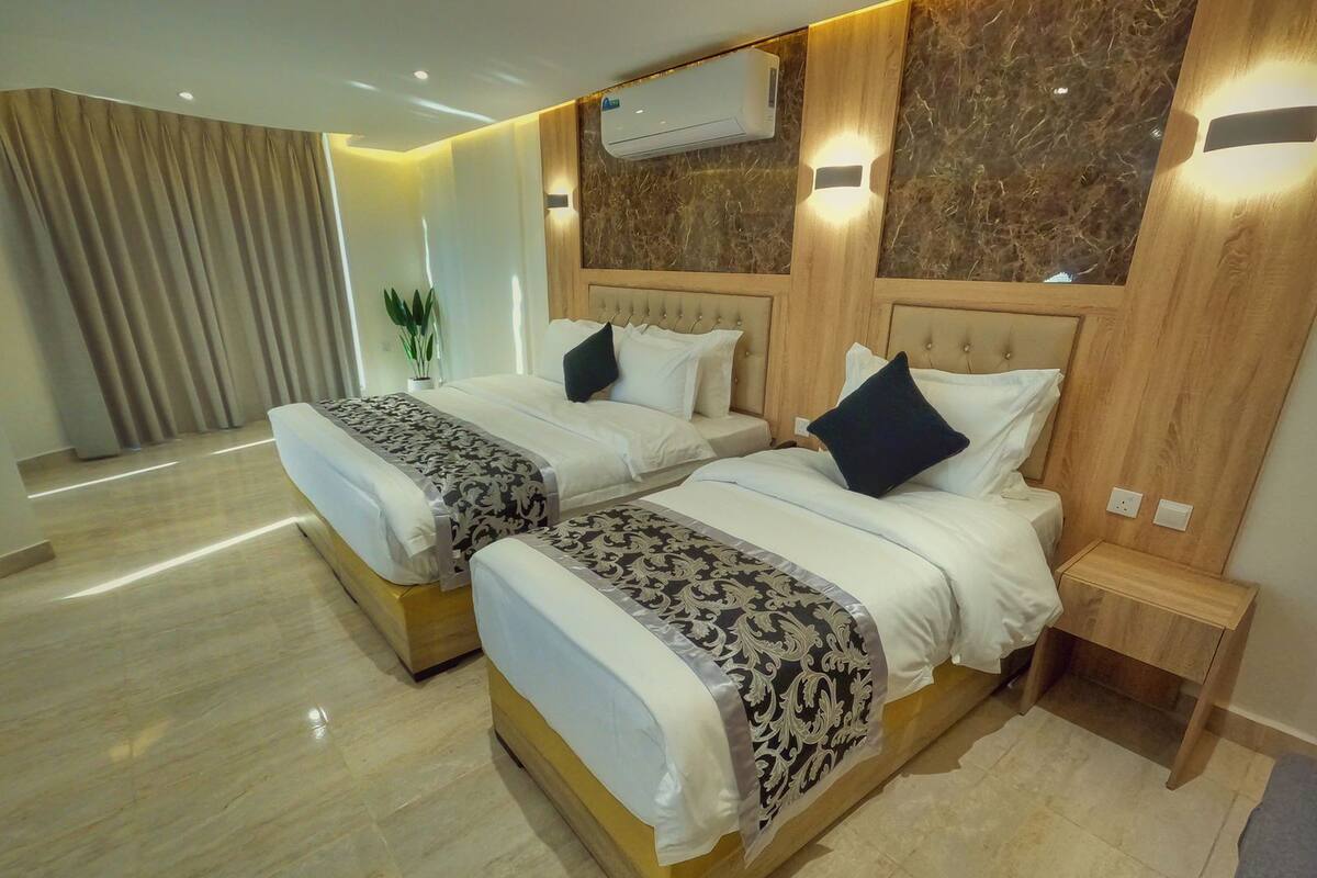 Habitación de hotel con dos camas, un muro con diseño de mármol, un equipo de aire acondicionado y una mesita de noche pequeña.