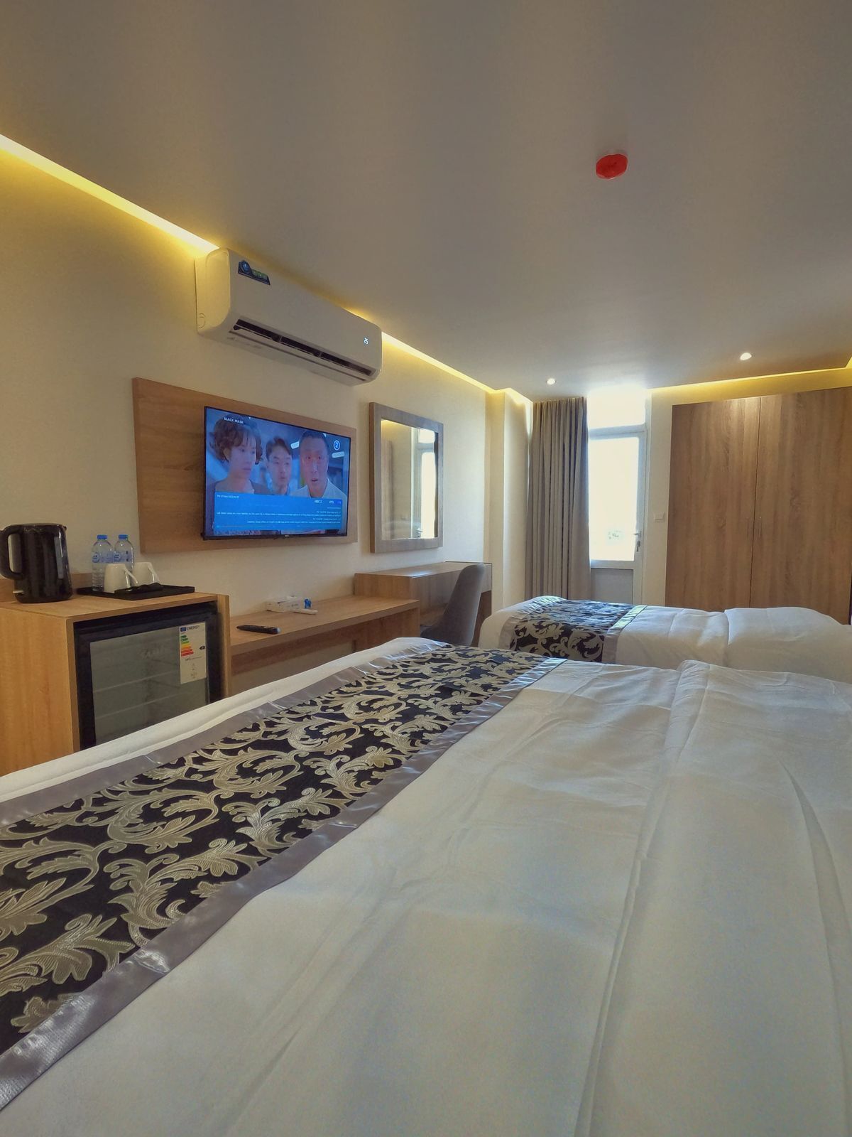 A hotel room with a bed, a desk, a television, and an air conditioning unit.