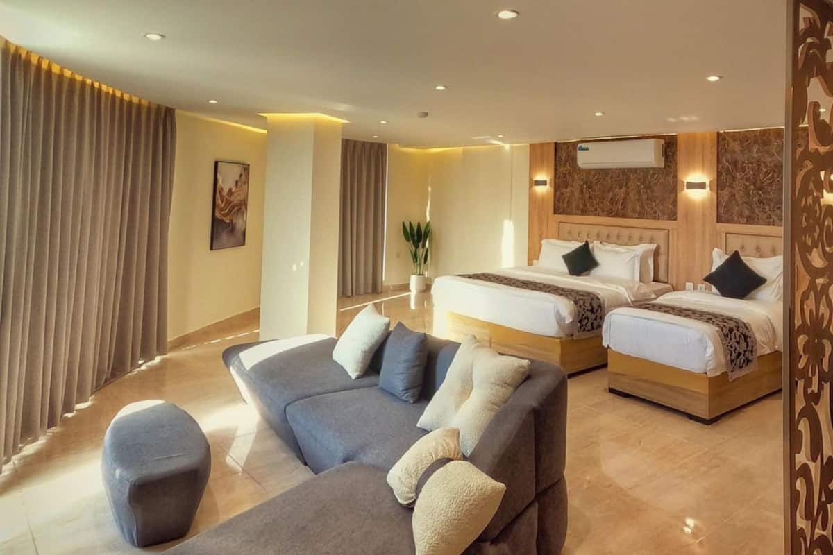Una habitación de hotel moderna con un sofá grande, dos camas y un panel decorativo en la pared.