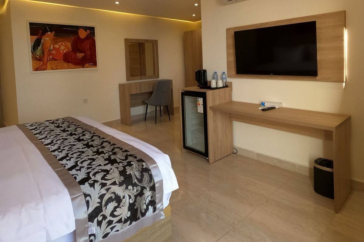 Una habitación de hotel con cama, escritorio, televisor y aire acondicionado.