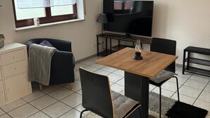Una sala de estar moderna con una mesa de comedor de madera, sillas negras, un sofá, un televisor y un reloj en la pared.