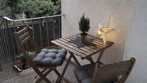Una mesa de madera con dos sillas, una planta pequeña en maceta y un farol con forma de estrella en un balcón.