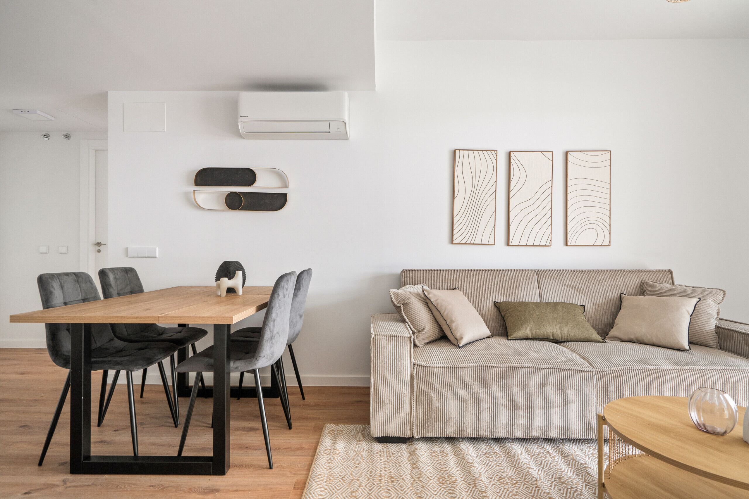 Una sala de estar moderna con una mesa de comedor de madera, sillas negras, un sofá a rayas y una alfombra estampada.