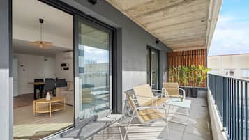 Un balcón con una zona de estar, una puerta de cristal que da a una sala de estar y plantas en macetas.