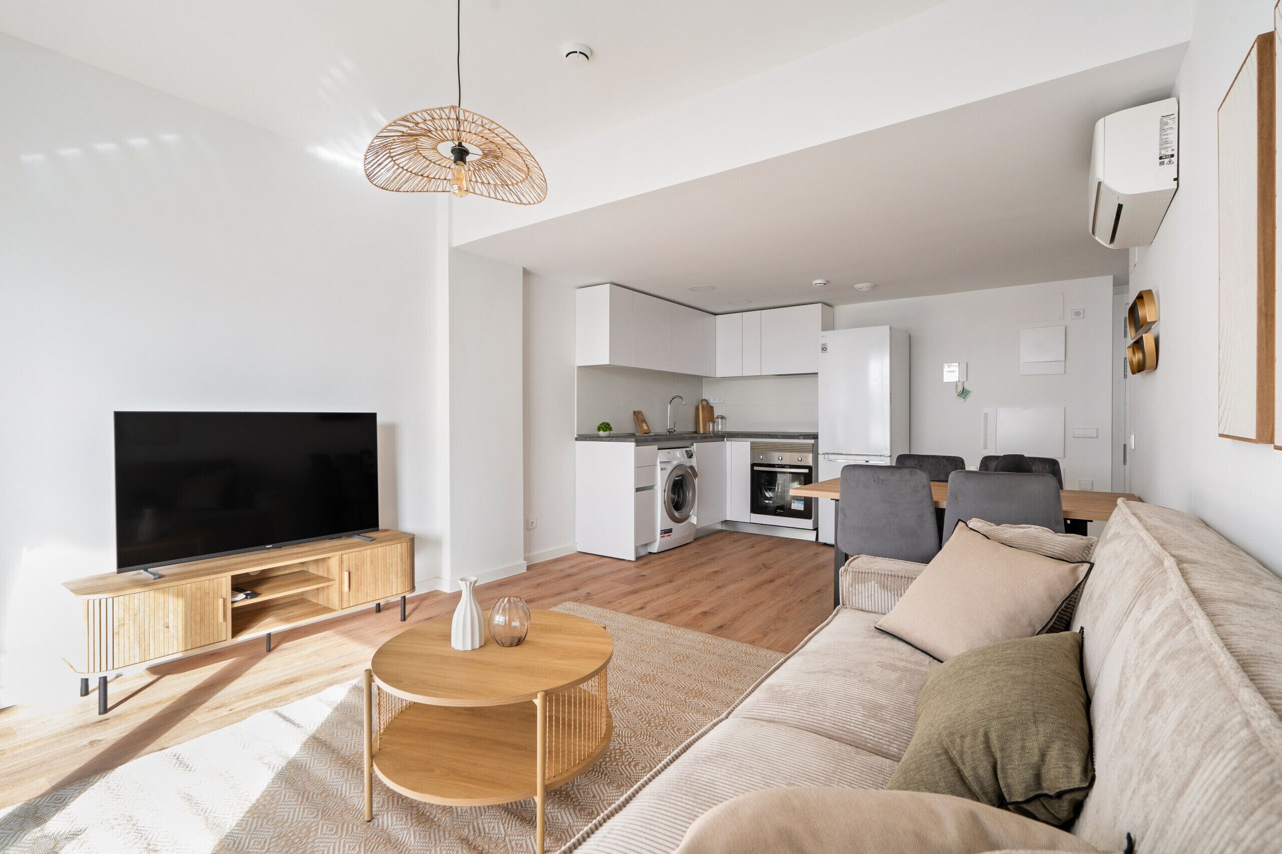 Ein modernes Wohnzimmer mit Flachbildfernseher, Holzmöbeln, einem Essbereich und einer Küche im Hintergrund.
