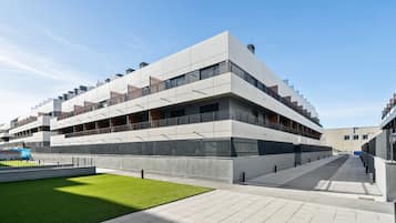 Un edificio moderno de varios pisos con techo plano, ventanas amplias y un patio central con césped verde.