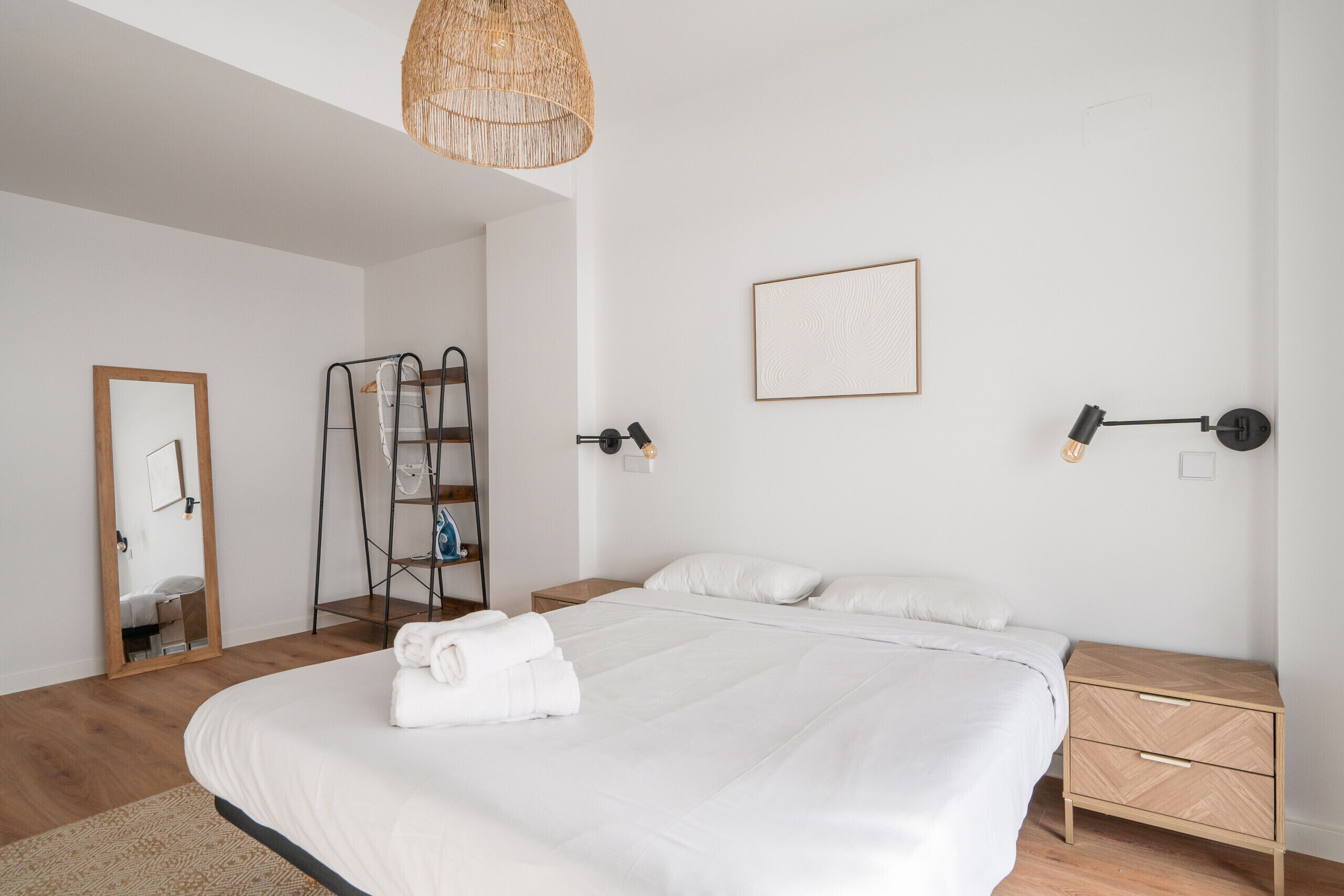 Un dormitorio moderno con una cama grande, una mesita de noche de madera, un estante montado en la pared y una lámpara colgante.