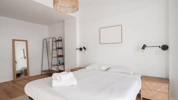 Un dormitorio moderno con una cama grande, una mesita de noche de madera, un estante montado en la pared y una lámpara colgante.