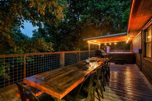 An outdoor deck with a wooden table and chairs, surrounded by a metal fence and trees. - Luxury Fall Getaway! 15 MIN to Dollywood! Hot Tub! (Sevierville)