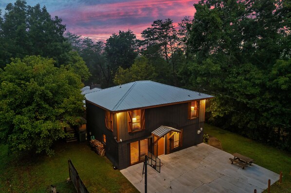 A modern two-story house with a metal roof, a covered patio, and a well-maintained lawn. - Luxury Fall Getaway! 15 MIN to Dollywood! Hot Tub! (Sevierville)
