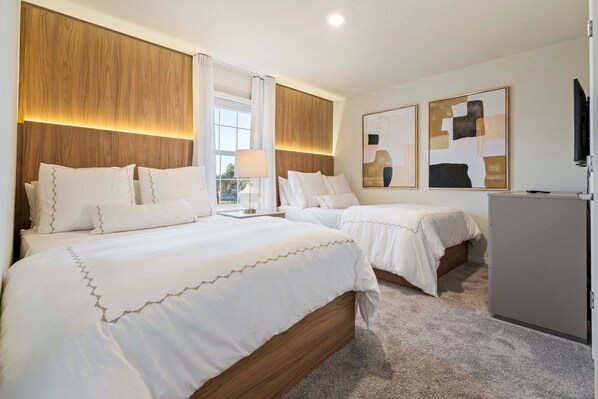 Une chambre d’hôtel avec deux lits, une tête de lit en bois, un téléviseur à écran plat et des œuvres d’art abstraites accrochées au mur.