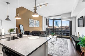 A modern kitchen with a large island, a dining area with a view, and a living space with a sofa and a TV.