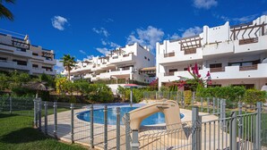 A residential building with a swimming pool surrounded by a fence, palm trees, and a clear blue sky. - Casa Ines (Mar de Pulpi) (San Juan de los terreros)