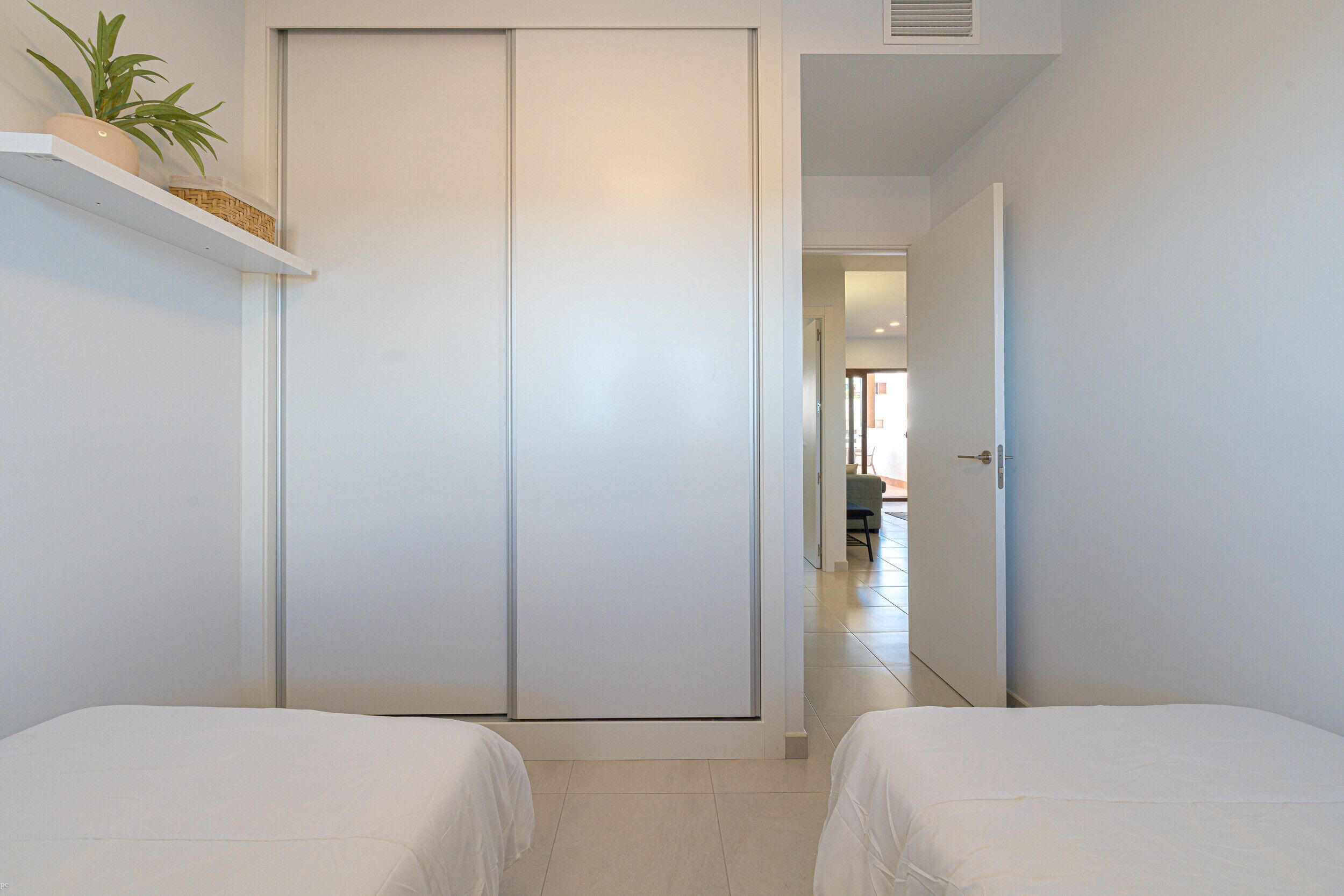 A hotel room with two beds, a sliding door closet, and a potted plant on a shelf.
