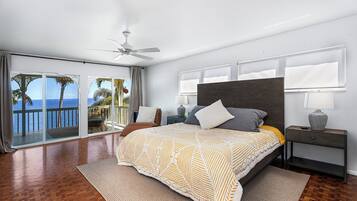A modern bedroom with a large bed, a ceiling fan, and a view of the ocean through large sliding doors.