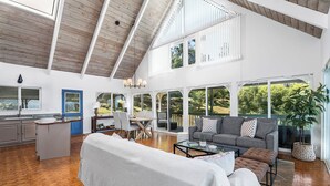 A spacious living area with a high ceiling, large windows, and a cozy seating arrangement.