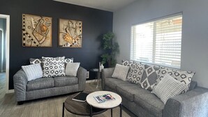 Un salon moderne avec deux canapés gris, des coussins à motifs, une table basse ronde et des œuvres d’art accrochées aux murs.