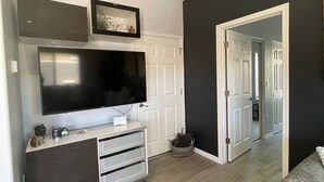 Un salon moderne avec un téléviseur à écran plat, un meuble de rangement pour appareils électroniques de couleur sombre et un canapé gris.