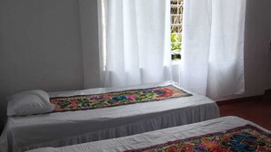 Two single beds with white linens and colorful embroidered bedspreads in a room with white curtains and a window. - CASA TURISTICA VALERIANA (Cali)