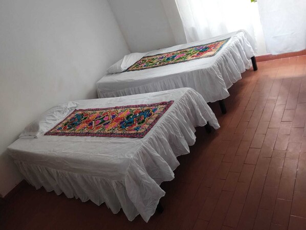 Two beds with white covers and colorful embroidered runners, in a room with tiled flooring and white walls. - CASA TURISTICA VALERIANA (Cali)