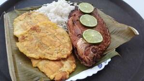 A plate with rice, fried plantains, and a grilled fish, garnished with lime slices. - CASA TURISTICA VALERIANA (Cali)