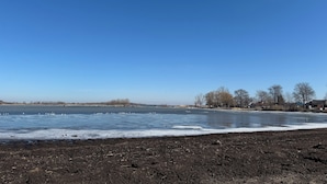 A frozen lake with a clear sky, surrounded by bare trees and distant buildings.
