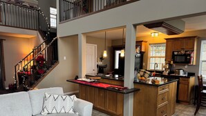 A modern kitchen with wooden cabinets, a central island, and a dining area with a grey sofa.