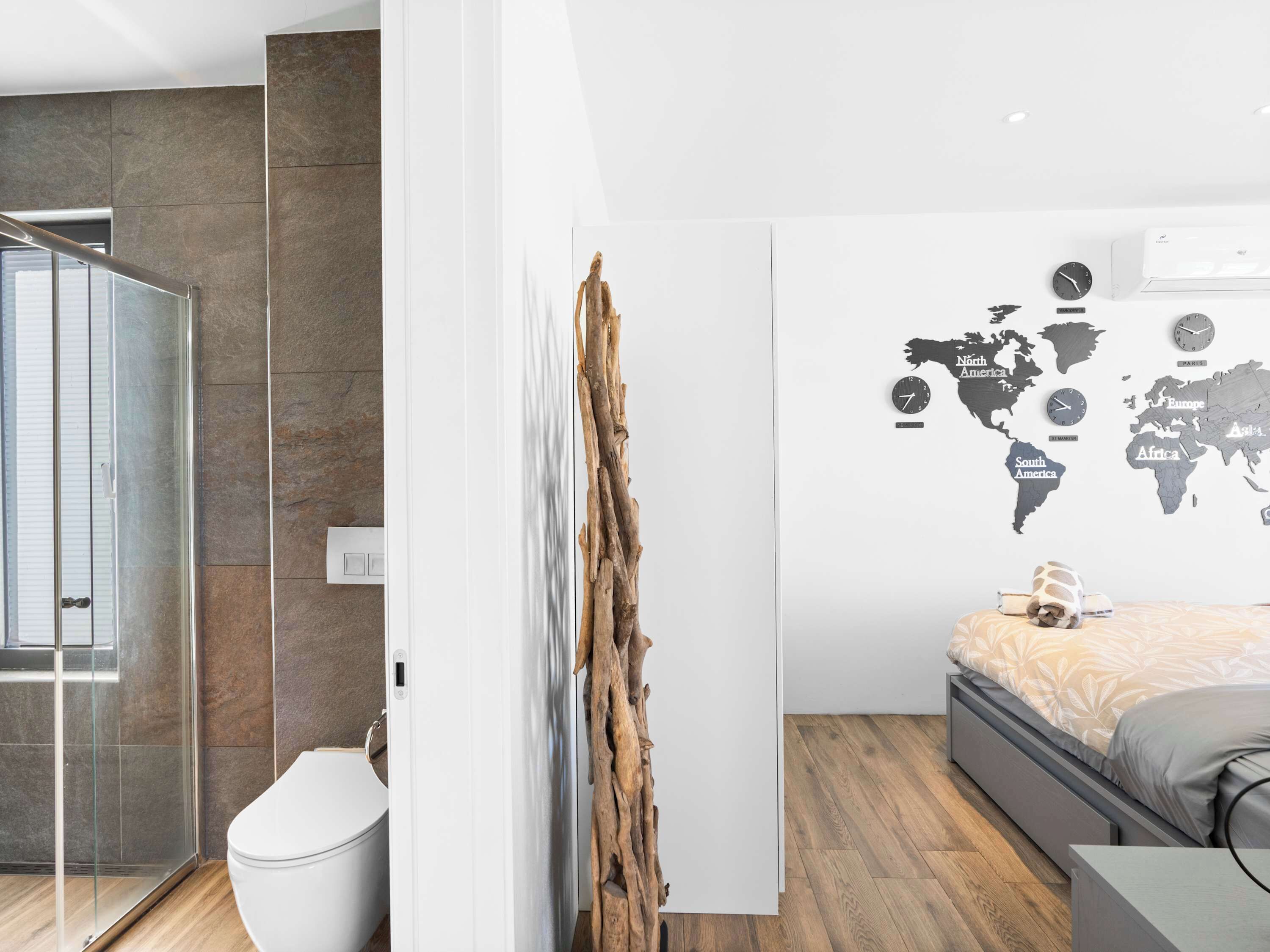 Ein modernes Schlafzimmer mit Bett, einer Weltkarte an der Wand, Holzboden und einer Duschkabine aus Glas.