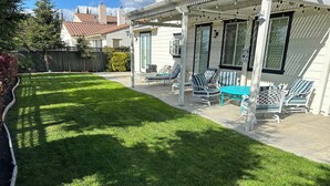 Eine Terrasse mit Gartenmöbeln, ein gepflegter Rasen und ein Haus im Hintergrund.