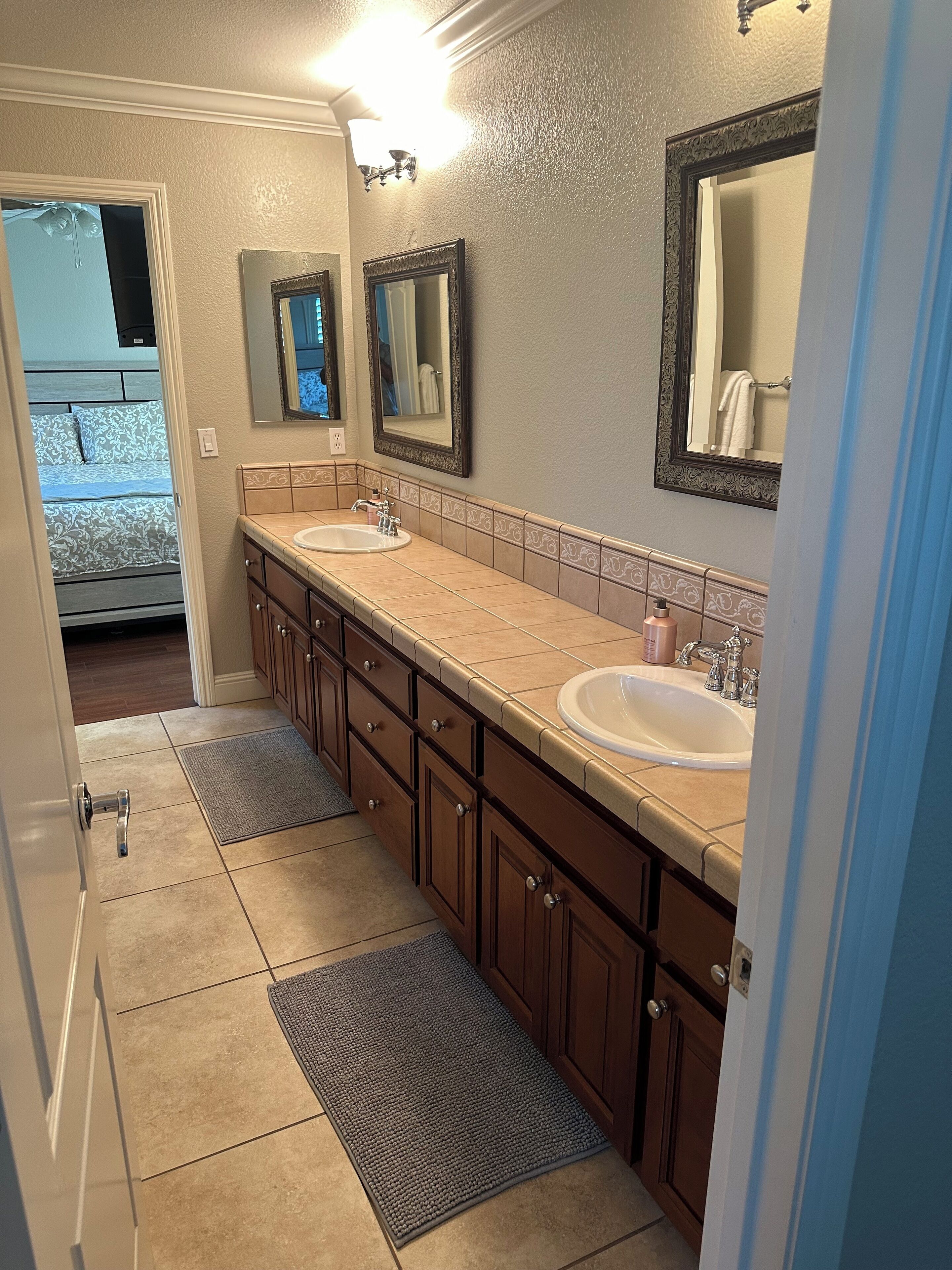 A bathroom with two sinks, a mirror, and a door leading to a bedroom.