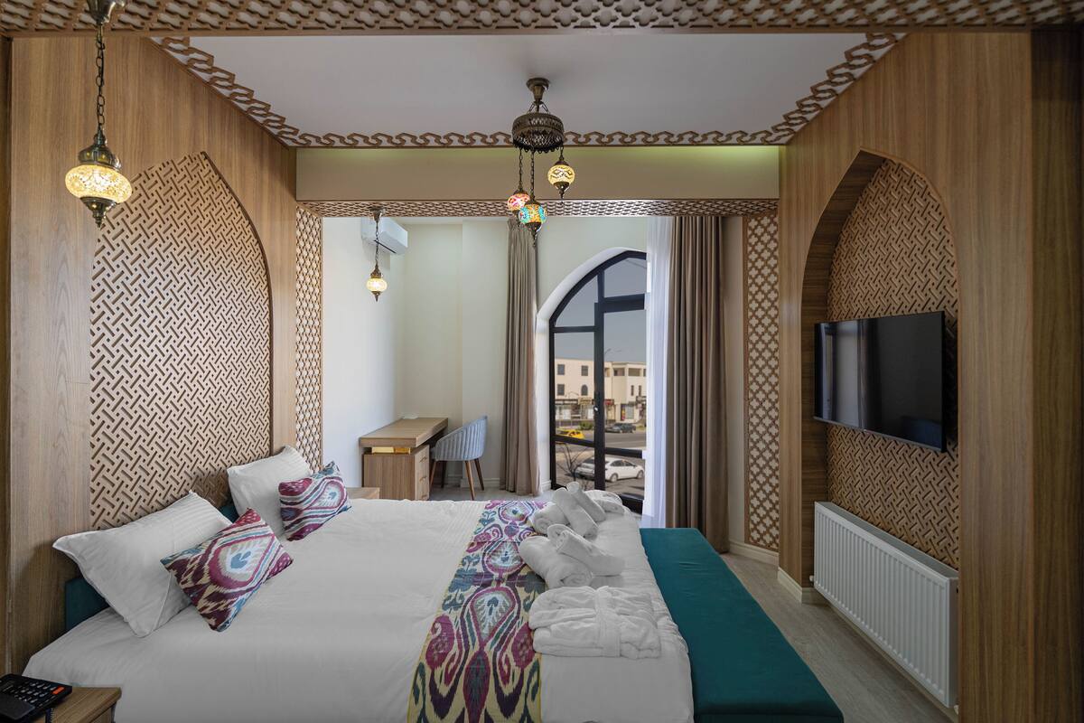 A hotel room with a bed, a desk, a chair, a TV, and a view of the outside.