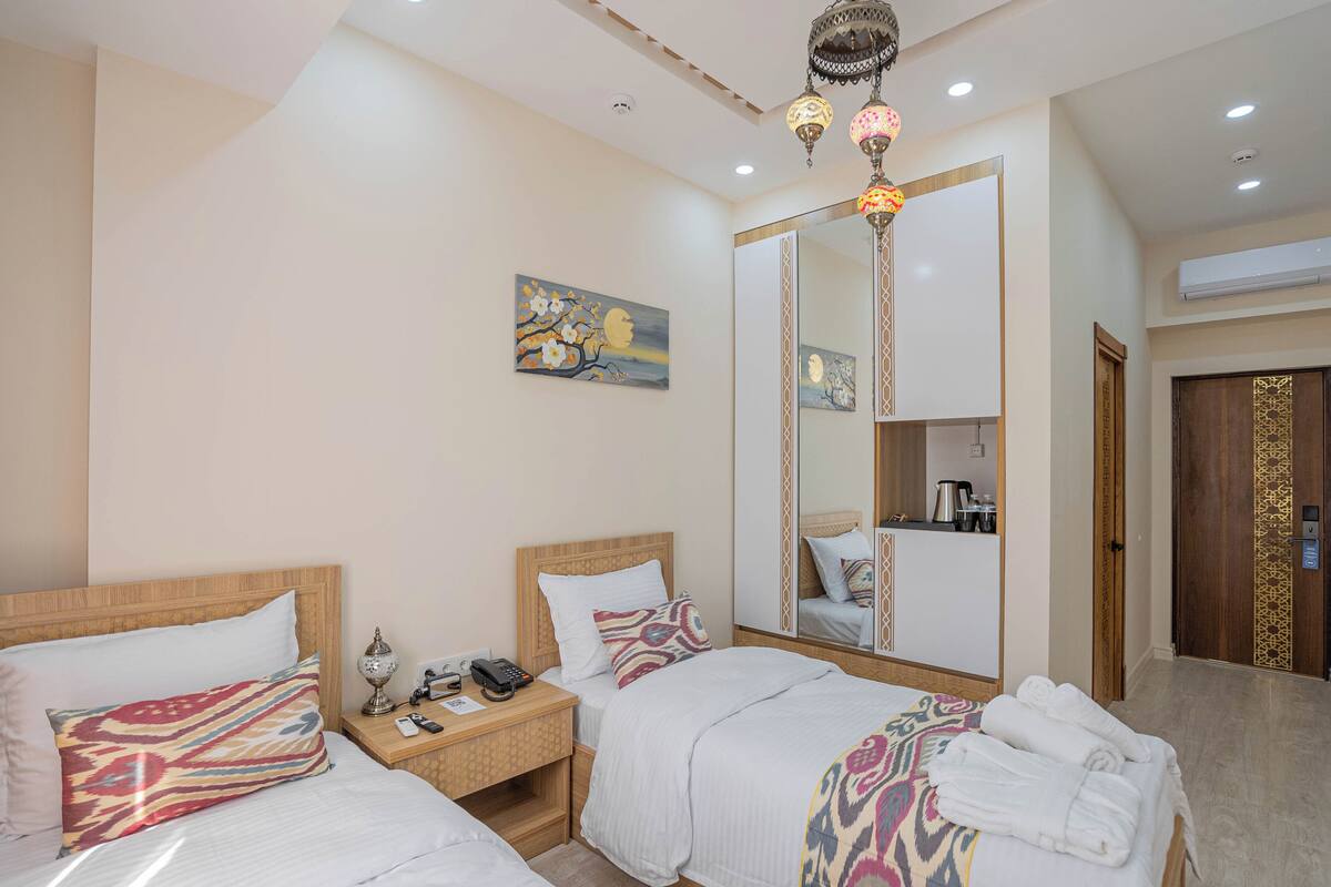 A hotel room with two beds, a nightstand, a telephone, a lamp, a mirror, and a painting on the wall.