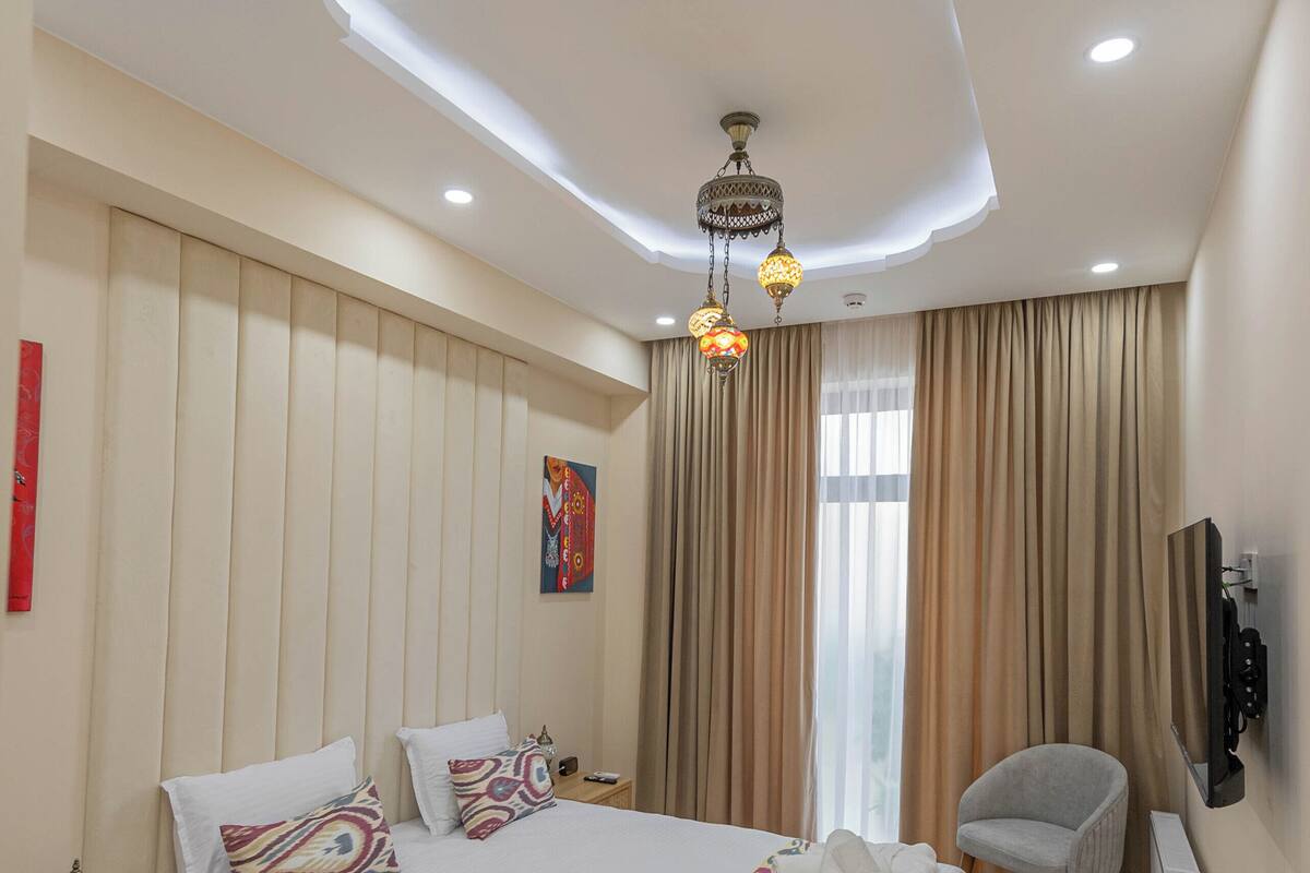 A hotel room with a large bed, a chair, a TV, and a ceiling with a unique design.