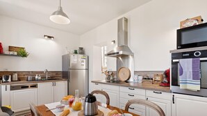 Une cuisine moderne avec des meubles blancs, des appareils en acier inoxydable et une table à manger en bois, accompagnée de chaises.