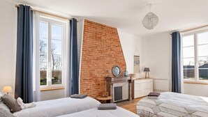 Une chambre avec deux lits, un mur en briques, une cheminée et une fenêtre avec des rideaux.