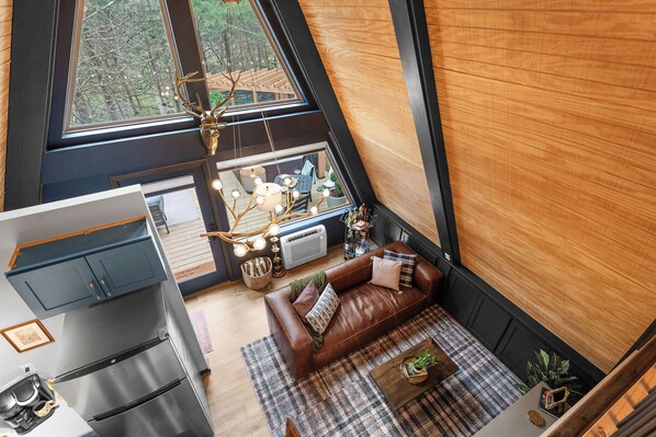 Een moderne loftkamer met een groot raam, een bruine leren bank, een eethoek en een keuken met een roestvrijstalen koelkast.