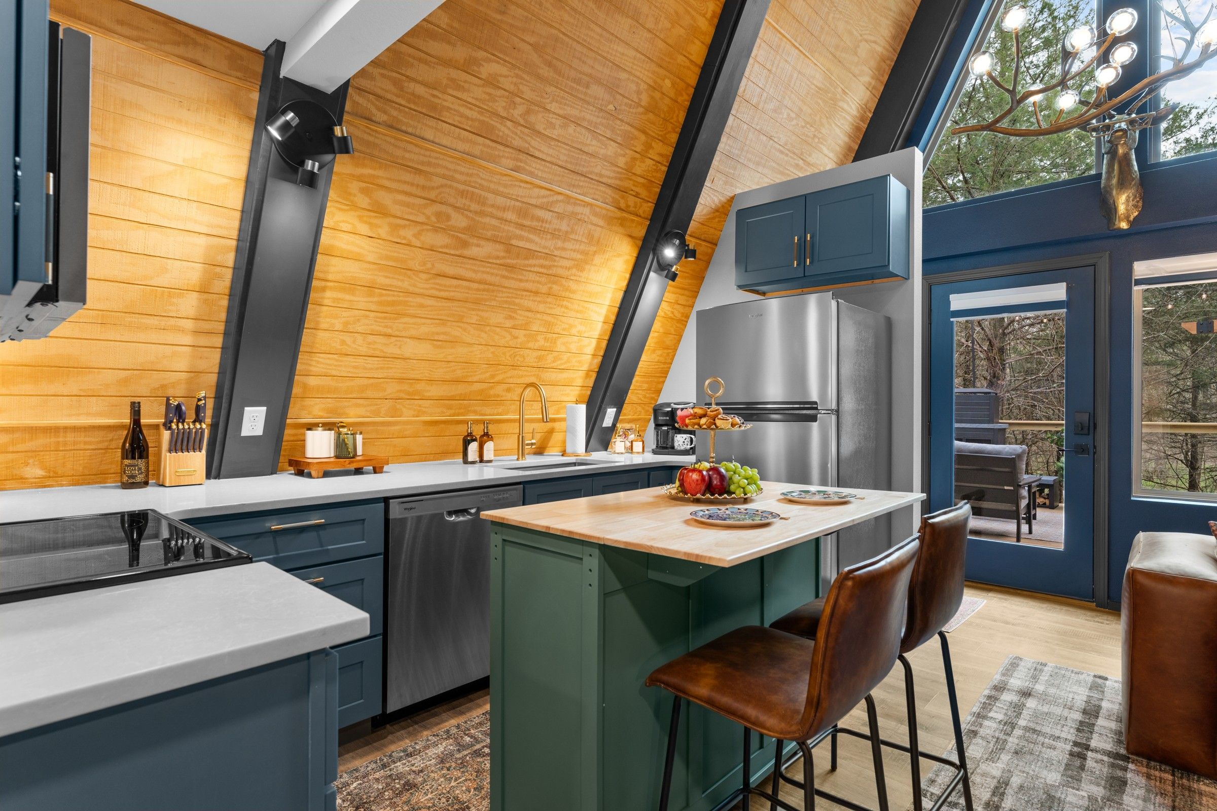 A modern kitchen with a central island, wooden ceiling, and a view through a large window.