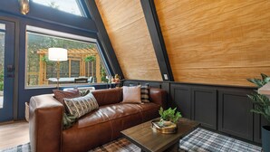 Ein gemütliches Wohnzimmer mit einer braunen Ledersofa, einem Holztisch und Blick auf eine Holzpergola draußen.
